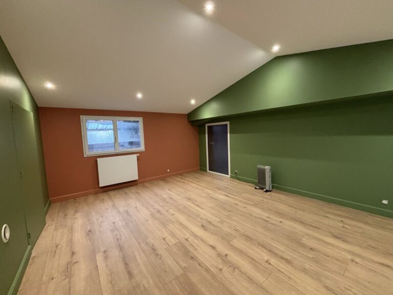 **Balise alt :** ``` Pièce rénovée sous combles avec murs bicolores vert olive et terracotta, parquet stratifié clair et spots encastrés, plafond en pente ``` --- **Variantes :** **Courte :** ``` Chambre ou bureau sous combles après rénovation, peinture vert et terracotta sur parquet clair ``` **SEO (peinture/rénovation intérieure) :** ``` Rénovation de combles en Normandie avec peinture murale bicolore vert olive et terracotta, parquet stratifié et éclairage encastré