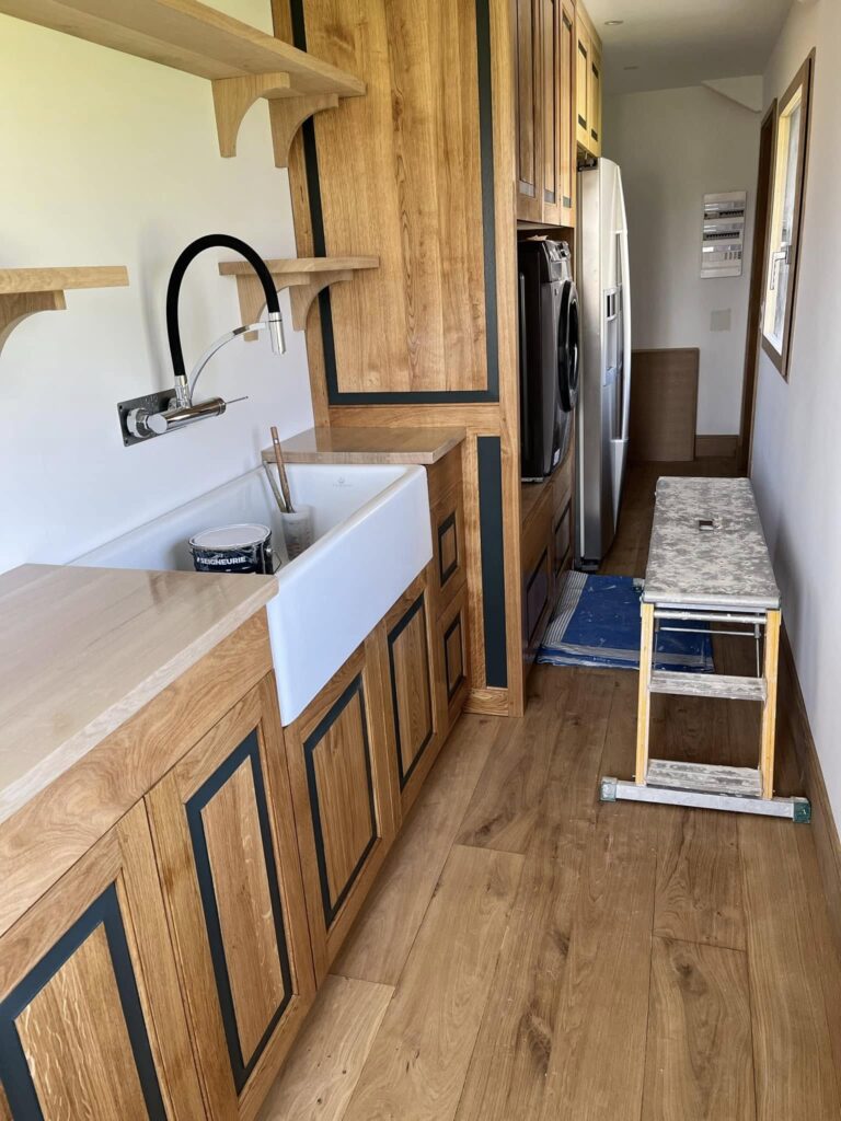 Cuisine artisanale en chêne massif avec évier à tablier blanc et robinet mural, rénovation en cours en Normandie