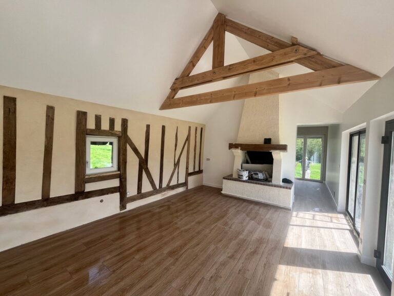 Grand séjour rénové avec colombages normands apparents, ferme de charpente en bois, cheminée en pierre blanche et carrelage imitation parquet, hauteur sous plafond cathédrale