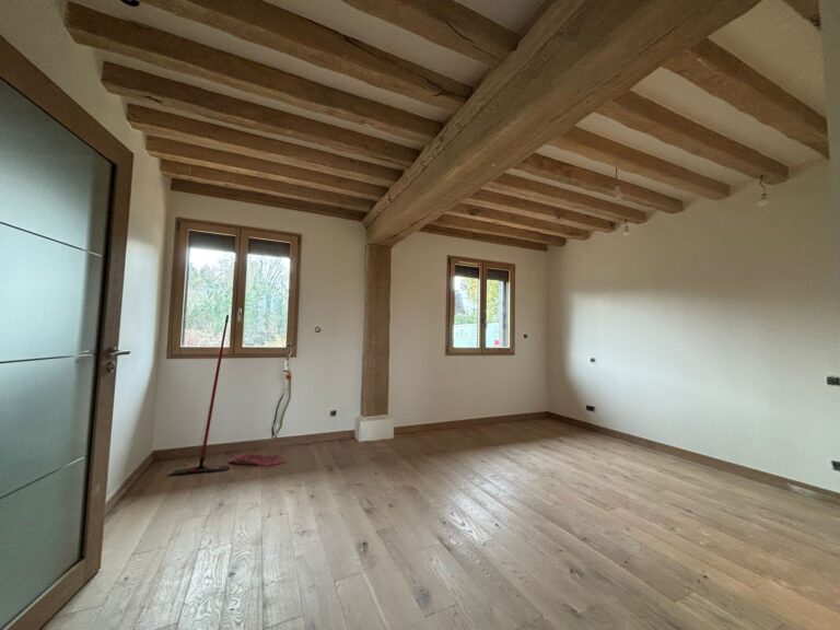 Rénovation intérieure en Normandie avec mise en valeur des poutres chêne apparentes, parquet massif et enduit blanc, finitions soignées