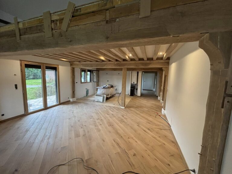 **Balise alt :** ``` Rénovation de grange ou maison ancienne en cours, grande pièce de vie avec charpente en bois apparent, poutres et colombages, parquet chêne massif et baie vitrée sur jardin ``` --- **Variantes :** **Courte :** ``` Chantier rénovation avec charpente bois apparente, parquet chêne et baie vitrée, pièce de vie en cours de finition ``` **SEO (rénovation/construction bois) :** ``` Rénovation d'une bâtisse normande avec charpente en chêne apparent, parquet massif et grandes ouvertures sur jardin, chantier en fin de travaux