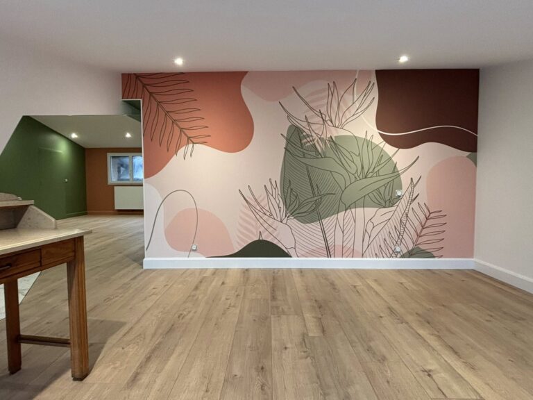 **Balise alt :** ``` Pièce rénovée avec papier peint panoramique motifs botaniques tons terracotta, rose et vert olive, parquet stratifié clair et mur d'accent vert sauge visible en arrière-plan ``` --- **Variantes :** **Courte :** ``` Papier peint panoramique botanique terracotta et vert olive sur parquet clair, pièce après rénovation ``` **SEO (contexte peinture/décoration intérieure) :** ``` Rénovation intérieure en Normandie avec pose de papier peint panoramique botanique, tons terracotta et vert olive sur parquet stratifié